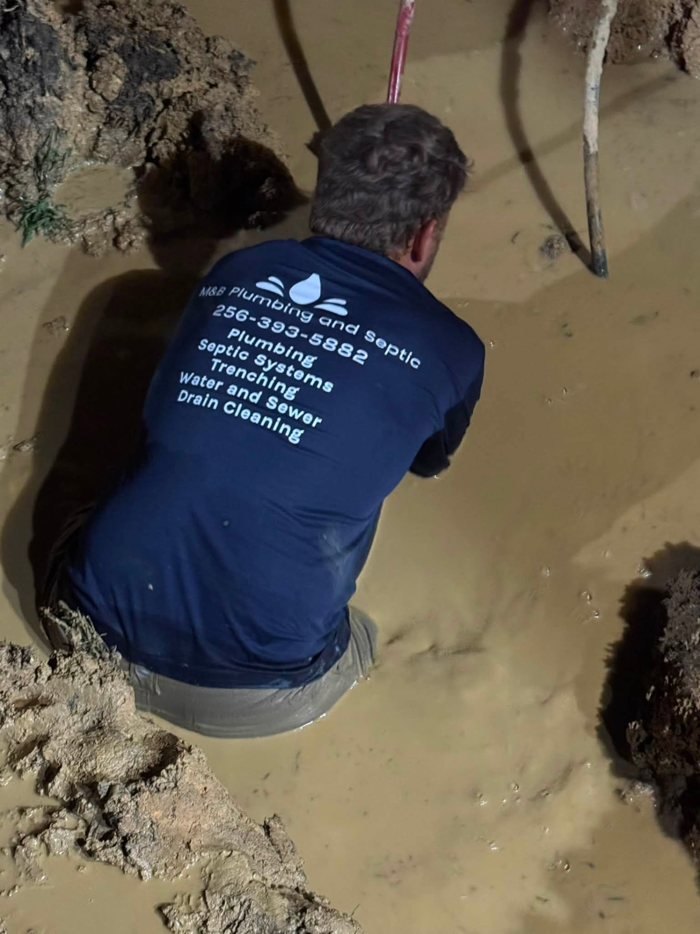 M&B Plumbing and Septic technician working in a muddy trench repairing an underground water and sewer line